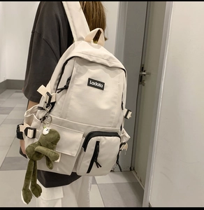 Detail view of cream nylon backpack with multiple functional pockets and cute frog pendant