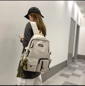 Detail of cream canvas backpack with functional pockets and a cute frog charm