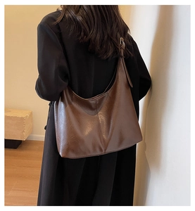 Detail view of large dark brown hobo shoulder bag with fine leather texture on black coat