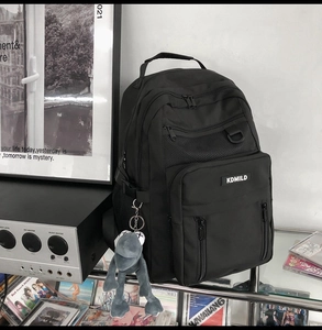 Close-up of black nylon backpack with multi-layer zippers and creative plush frog pendant