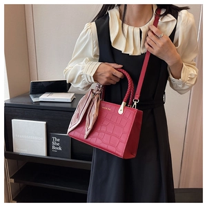 Detail of red crocodile textured leather handbag with a braided handle and printed silk scarf