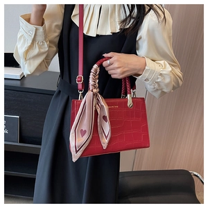 Detail view of red crocodile texture handbag with decorative scarf and gold logo hardware
