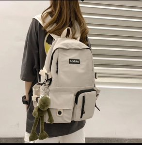 Detail of a large-capacity cream nylon backpack with multi-pockets and a green frog pendant
