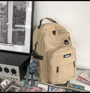 Detail view of khaki multi-compartment backpack with mesh pockets and plush charm