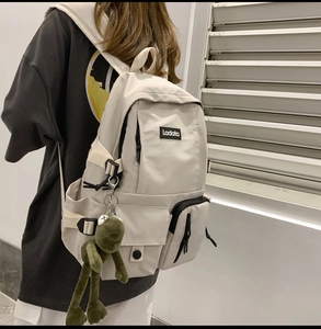 Detail of off-white waterproof nylon backpack with a green plush frog charm pendant