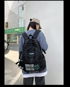Detailed outdoor view of a black nylon backpack with multi-pocket design and trendy charms