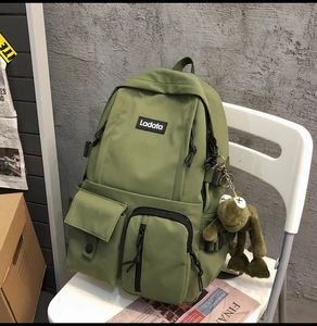 Detail of army green nylon backpack with multi-pockets and a cute green frog pendant