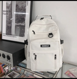Detail view of white minimalist backpack with front pockets and logo on a glass desk