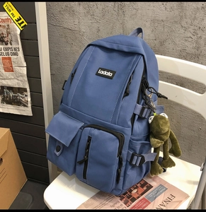 Blue canvas backpack with multiple pockets and cute frog charm on a chair