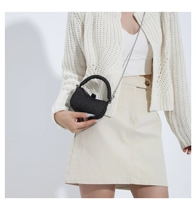 Detail of black tweed mini chain bag showing texture and arc handle against white knit