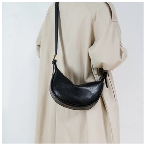 Detailed view of the black leather hobo bag worn by a model in a beige trench coat