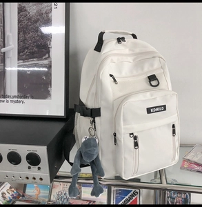 Close-up of white multi-pocket backpack with mesh pockets and grey plush frog charm