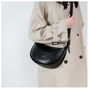 Detailed view of black faux leather crescent bag styled with a beige trench coat