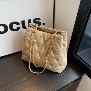 Quilted beige faux leather tote bag with gold chain straps on a wooden surface