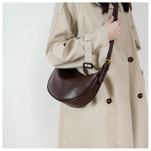 Detail view of large dark brown crescent moon leather bag worn with a beige trench coat