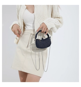 Mini navy denim crossbody bag with silver chain strap shown on a white knit cardigan