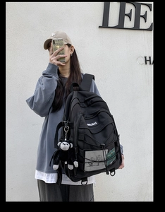 Close-up of black canvas backpack with mesh pocket, elastic cords and monkey plush charm
