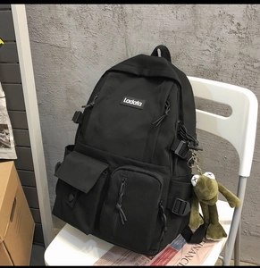 Detailed view of a black utility backpack with multiple pockets and a green frog pendant