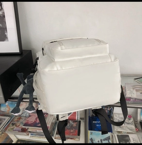 Detailed view of white nylon backpack with plush charm on a shelf with CD accessories