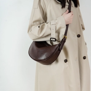 Minimalist dark brown crescent leather shoulder bag worn with a classic beige coat