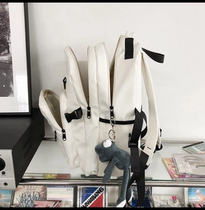 Detail view of white multi-layer backpack featuring side buckles and cute frog plush charm