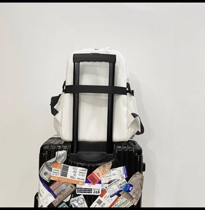 White nylon backpack detail showing travel luggage strap and side mesh pocket features