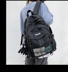 Detail of black nylon backpack featuring mesh compartment, crisscross ropes and monkey charm