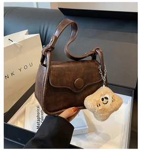 Detail of vintage brown mini leather bag with round buckle and plush smiley charm in gift box