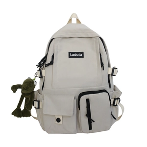 Minimalist cream canvas school backpack with Ladata logo and a green frog plush charm