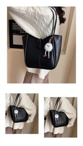 Detail of black faux leather tote bag with fluffy white charm and thin shoulder straps