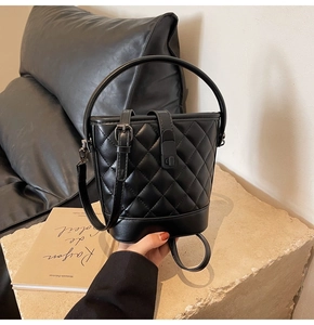 Detail of black quilted bucket bag with leather texture and elegant top handle on stone