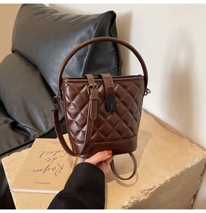 Detail of a brown quilted bucket bag with a glossy finish on a textured stone surface
