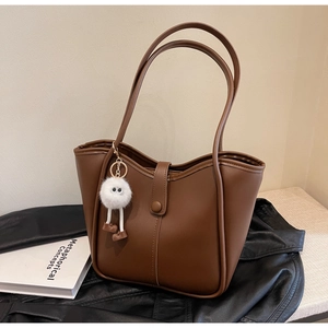 Detail of deep brown leather tote bag with wavy top edge and cute plush monster charm