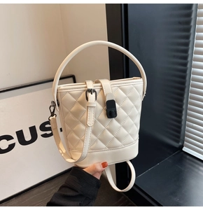 Detailed view of beige quilted bucket bag with circular handle and black clasp buckle