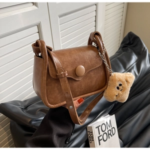 Close-up of vintage brown PU leather crossbody bag with wave flap and plush charm