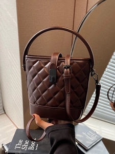 Quilted dark brown leather bucket bag with top handle and crossbody strap displayed in hand