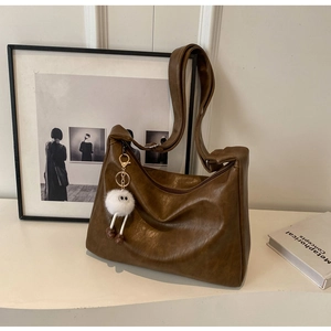 Detailed close-up of brown vintage leather hobo bag texture with a cute plush monster charm