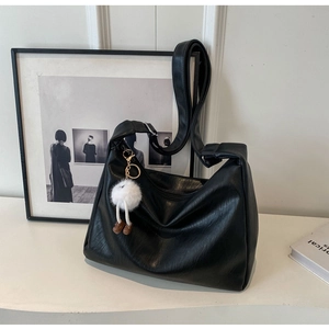 Detail of soft black leather shoulder bag featuring a cute plush doll pendant charm