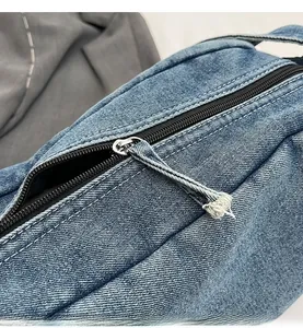 Detail of smooth black zipper and denim strap on blue diagonal weave texture bag