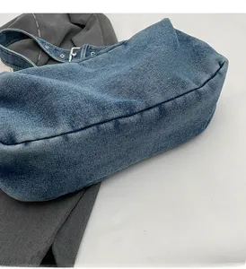Detail view of washed blue denim shoulder bag with adjustable metal eyelet strap