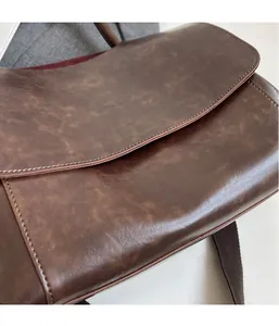 Close-up of vintage brown messenger bag with contrast stitching and wide fabric strap