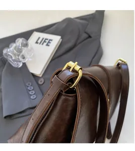 Détail d'un sac bandoulière marron foncé avec boucle dorée réglable et bandoulière