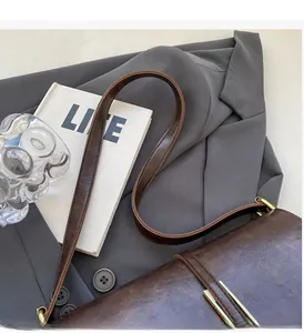 Détail d'un sac à bandoulière en cuir marron vintage avec garniture dorée sur costume