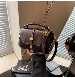 Detail of dark brown retro handbag featuring golden buckle and smooth leather texture
