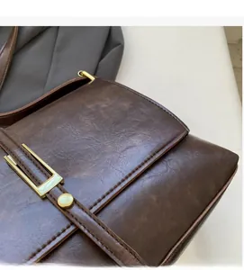 Détail de la texture cuir marron vintage et boucle dorée sur le sac à bandoulière