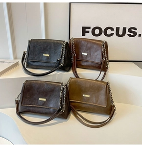 Detail of four colorful leather tote bags with gold chain straps on display stand