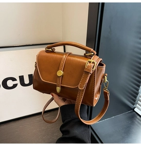 Detail of a brown leather crossbody bag with metal buckle and cylindrical top handle