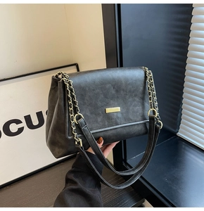 Detail of matte black leather handbag featuring a gold buckle and metal chain strap