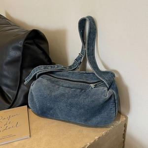 Blue washed denim shoulder bag with adjustable eyelet strap on stone surface