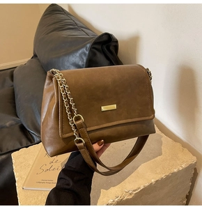 Detail of dark brown leather bag with gold metal trim and chain strap on stone stand
